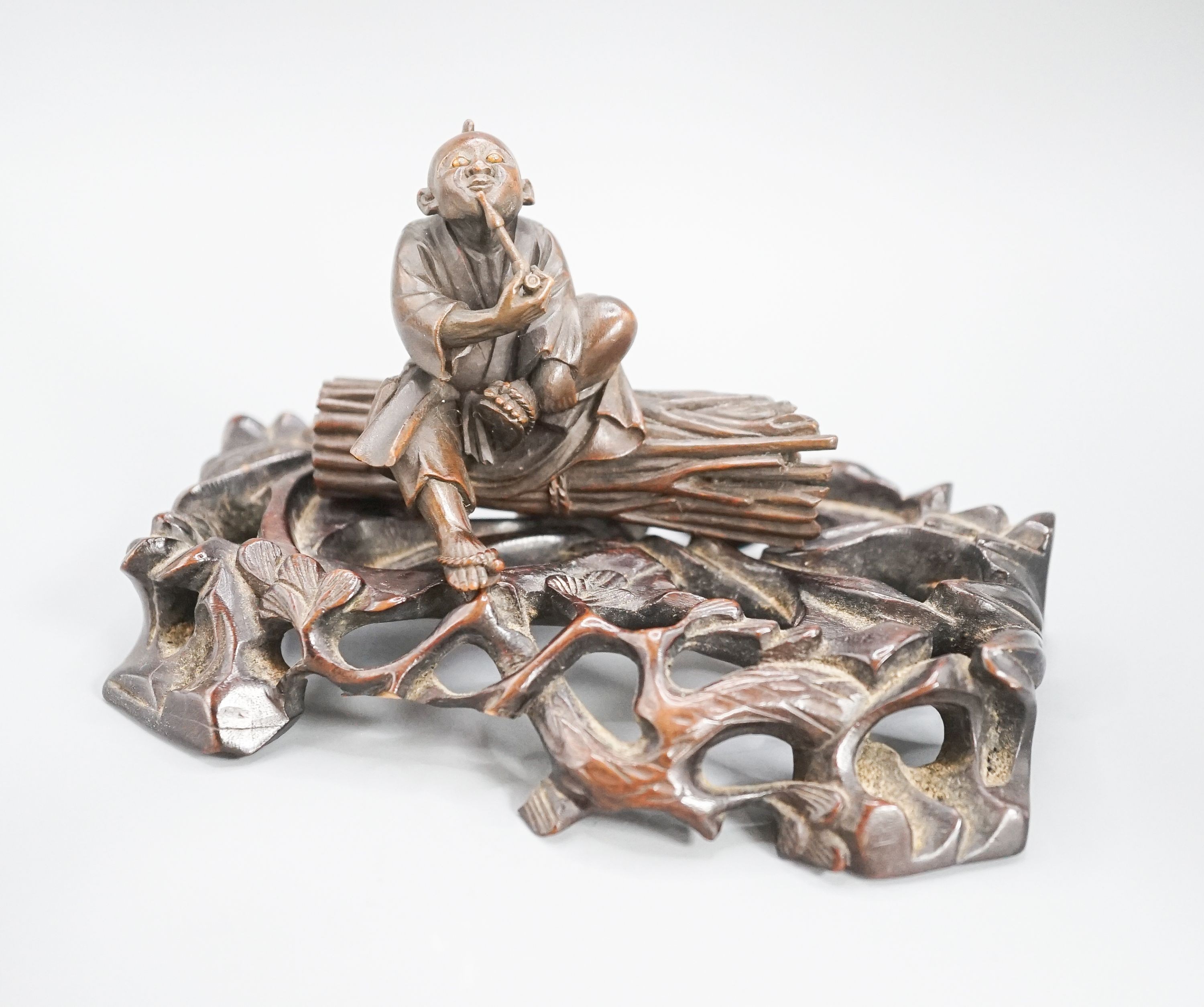A 19th century Japanese wood okimono of a seated man smoking a pipe, signed, 7.8cm on a later hardwood stand